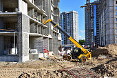 Telescopic handler work at the construction site. Construction machinery for loading. Tower crane during construct a multi-storey residential building. Wheel loader for lifting goods